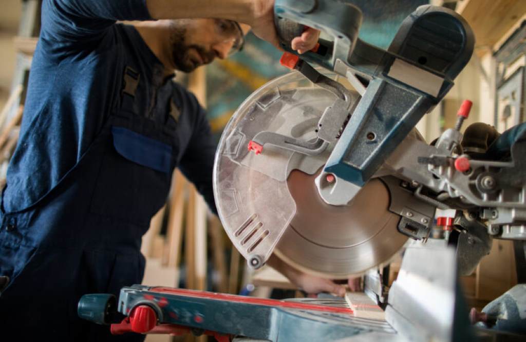 Safety goggles, gloves, and blade guard highlighted next to a miter saw in active workshop setup.
