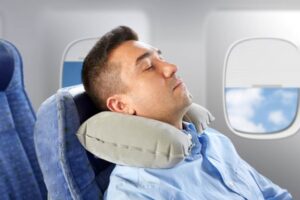 Traveler sleeping peacefully on plane with Dot&Dot Twist Pillow shaped around neck and window