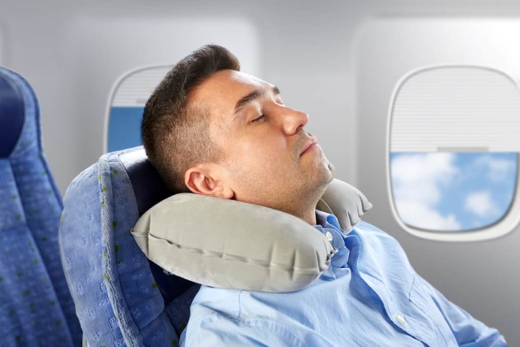 Traveler sleeping peacefully on plane with Dot&Dot Twist Pillow shaped around neck and window
